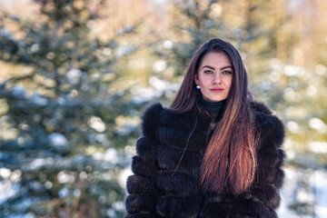 cheerful young female in a warm fur coat enjoying a winter day in the snowy forest