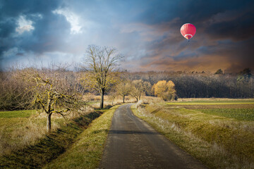 a red hot air balloon hovering over a country highway