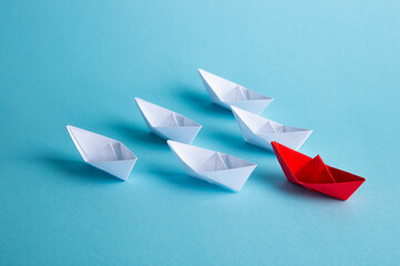 Red leader paper ship leading among others on blue background. Leadership concept.