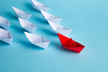 Red leader paper ship leading among others on blue background. Leadership concept.