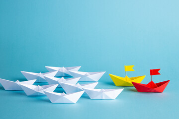 Red leader paper ship leading among others on blue background. Leadership concept.