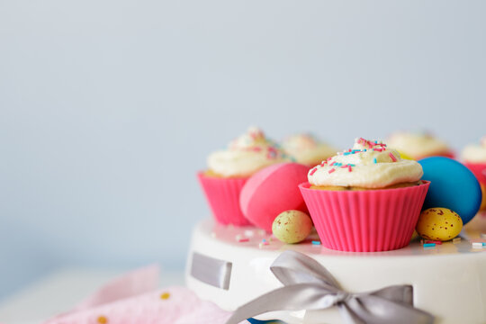 Easter sweets and decorations - close up of cupcakes and colorful painted eggs over white wall with copy space