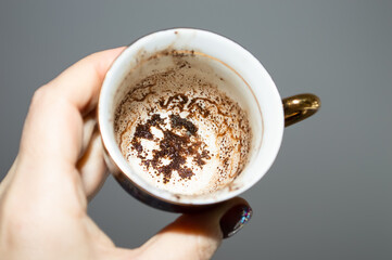 close-up - a cup with patterns of coffee grounds in a female hand on a gray background