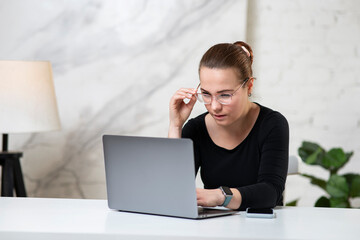 Young concentrated focused girl, serious beautiful woman in glasses is typing, working on her...