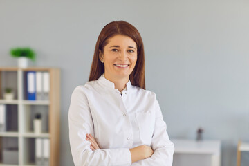 Happy positive woman in lab coat standing arms folded looking at camera. Portrait of reliable...