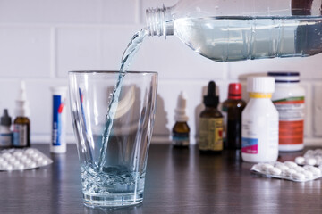 Pour water into a glass against the background of pills and medications. Clean water, liquid streams. Water from the bottle is poured into a glass.