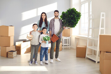 Fototapeta na wymiar Portrait of happy smiling young family with little children standing in their spacious new home with unpacked boxes on moving day. Concept of buying house or apartment, real estate, and mortgage