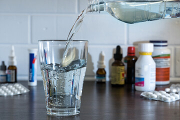 Pour water into a glass against the background of pills and medications. Clean water, liquid streams. Water from the bottle is poured into a glass.