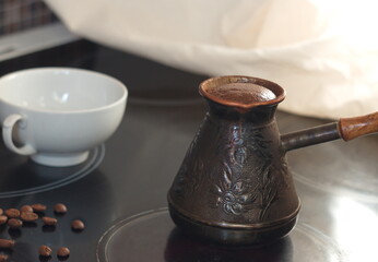 Natural aromatic coffee with froth is brewed in a Turk, there is a white mug next to it and coffee beans are scattered
