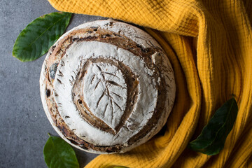 Sourdough bread with leaf pattern on the top, nuts, red apples, olives, raisins top view photo. Red textured background. Healthy living concept. 
