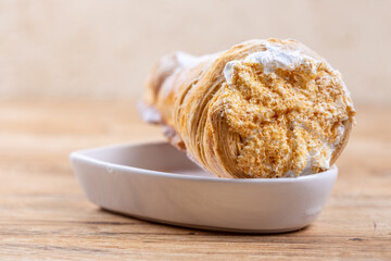 Delicious puff pastry cone with protein cream or whipped cream on wooden table