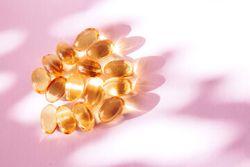 Shiny yellow fish oil capsules on a light background with shadows of focus on the table. Vitamin E....
