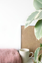 Breakfast still life. Cup of coffee, nude sweater, blank beige poster frame and indoor evergreen potted plant on the white wall. Scandinavian working space, home office