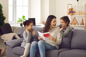 Little kids making surprise for mommy. Excited young woman thanking her children for handmade card on Happy Mother's Day. Cute twin daughters clapping hands and wishing their mom love and happiness