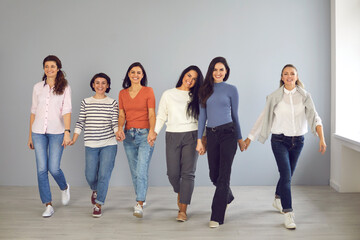 Fototapeta na wymiar Group of happy confident young women in their 20s and 30s smiling and looking at camera while walking together hand in hand ready to support each other. Concept of power, success and female solidarity