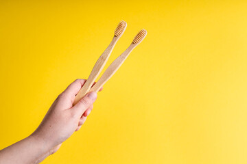 Female woman hand holding two Bamboo organic toothbrushes for dental hygiene on trendy yellow background - Eco-friendly zero waste plastic free concept Biodegradable material copy space