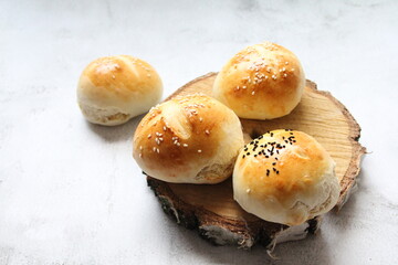 fresh rolls, bread stacked on a piece of wood, light wheat bread, homemade flour pastries, buns sprinkled with white and black sesame seeds