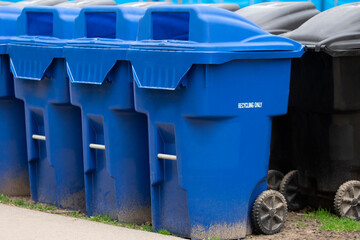 Large blue plastic garbage trash bins with sign recycling only standing upright arranged in a row in a city park. Selective focus. Clean city, environment consciousness concept.