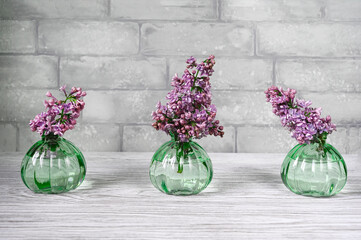 Lilac flowers in vases on a table against grey brick wall.