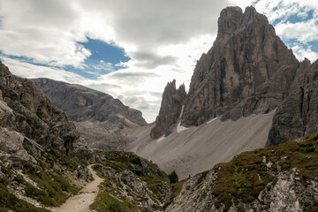 Obraz premium A panoramic view on Italian Dolomites. There are many high and sharp peak in front, with many landslides. Dangerous climbing. Barely any plants growing in the area. Raw and unspoiled landscape.
