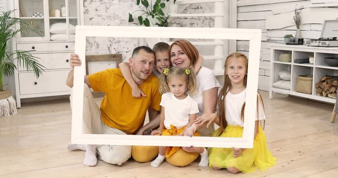 large happy family holding picture frame and smiling. the whole family is wearing white and yellow T-shirts. parents and children have time together