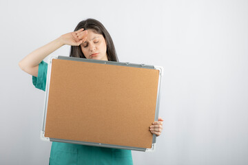 Tired young medical worker holding board with hand