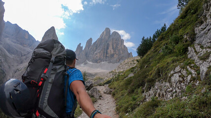 A man with big backpack taking a selfie while hiking along a narrow pathway in Italian Dolomites....