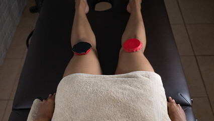 Brunette woman lying on a therapeutic stretcher with biomagnetism therapy magnets placed on her legs to treat her health with holistic therapies and alternative medicine