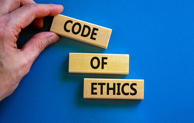 Code of ethics symbol. Concept words 'Code of ethics' on wooden blocks on a beautiful blue background. Businessman hand. Business and code of ethics concept. Copy space.