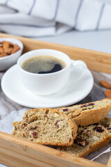 Close up Italian biscotti cookies on a tray and blurred cup of coffee on background. Fresh baked cookies with nuts and dried cranberries with selective focus