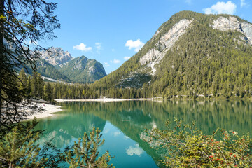 Fototapeta na wymiar A view on the Pragser Wildsee, a lake in South Tyrolean Dolomites. High mountain chains around the lake. The sky and mountains are reflecting in the lake. Dense forest at the shore. Autumn vibe. Relax