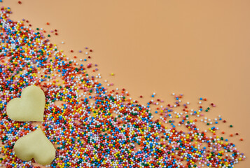 A mix of colorful sugar balls and hearts on a beige background with space for text. Festive background for Valentine's Day, March 8, birthday. Top view