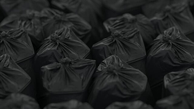 Rows of densely packed black trash bags move slowly in front of the camera. Depth of field.
