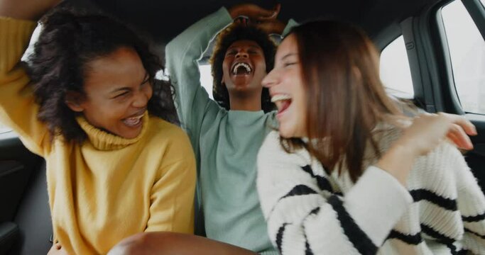 Diverse friends laughing and singing in
the backseat of a car
