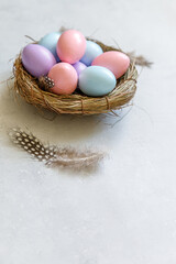 Happy Easter concept. Preparation for holiday. Colorful decorated easter eggs in nest with feather on concrete stone grey background. Simple minimalism flat lay top view copy space.