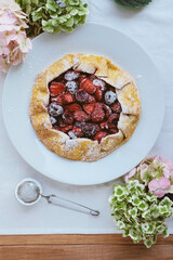 Fototapeta na wymiar Delicious freshly baked vegan strawberry and cherry galette on wooden rustic background with hydrangea flowers, close up. Sweet food, summer dessert.