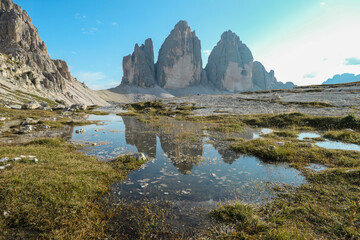 A panoramic view on the famous Tre Cime di Lavaredo (Drei Zinnen), mountains in Italian Dolomites. The mountains are reflecting in small paddle. Desolated and raw landscape. Natural phenomenon