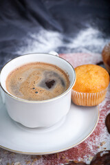 Black coffee with muffin in powdered sugar on a dark background