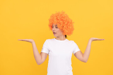amazed funny girl with fancy look wearing orange hair wig presenting product, copy space, choice.