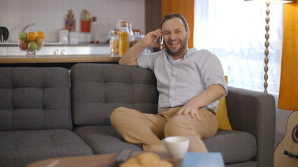 The young man talking on his mobile phone while sitting on his seat at home. The young man laughs at the person he is talking to on the phone.