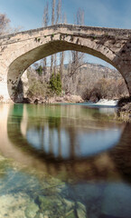 Fototapeta na wymiar Bridge of Roman origin with water with green and yellow tones and trees on the sides with blue sky with clouds in Ayende bridge in the Escabas river 