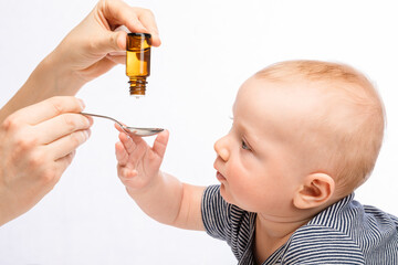 Mother feeding baby boy with drop of vitamin or liquid medicine from vial using spoon