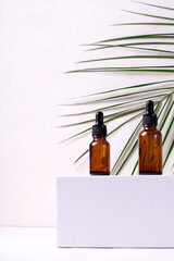 Glass dropper bottles on the white podium. Palm leaf in the background. Natural beauty products