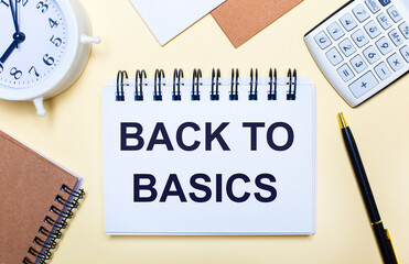 On a light background, a white alarm clock, a calculator, a pen and a notebook with the text BACK...