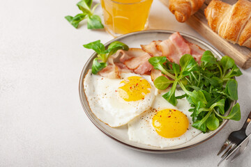 Continental breakfast - fried eggs, bacon and lettuce leaves in a plate on a bright background. Top View