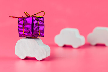 Gift delivery concept. Toy car delivers gift box on pink background. February 14 postcard, Valentine's Day, Christmas, New year, 
 March 8, international women's day. Minimalism style.