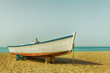 Fototapeta na wymiar A small wooden boat used by fishermen beached on the sandy beach next to the Mediterranean Sea