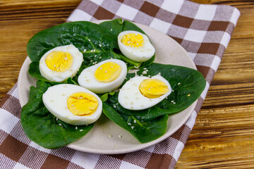 Boiled eggs with fresh spinach leaves and sesame seeds on wooden table