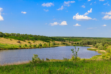 Summer landscape with beautiful lake, green meadows, hills, trees and blue sky