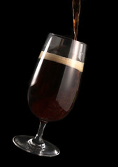 Beer is poured into a glass isolated on a black background